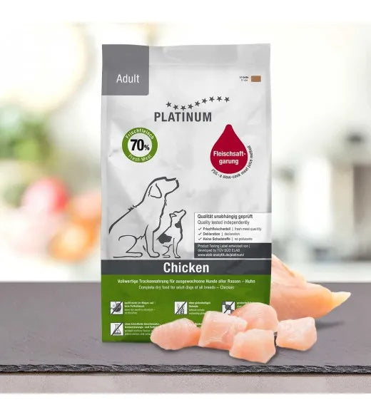 Platinum hundefoder med kylling til voksne hunde – næringsrigt tørfoder med 70% frisk kød. Posen viser en voksen hund og en hvalp, hvilket understreger, at foderet er letfordøjeligt og af høj kvalitet. I forgrunden ses friske kyllingestykker på en skiferplade, hvilket fremhæver de naturlige ingredienser. Perfekt tørfoder til hunde, der har brug for proteinrig og sund ernæring.