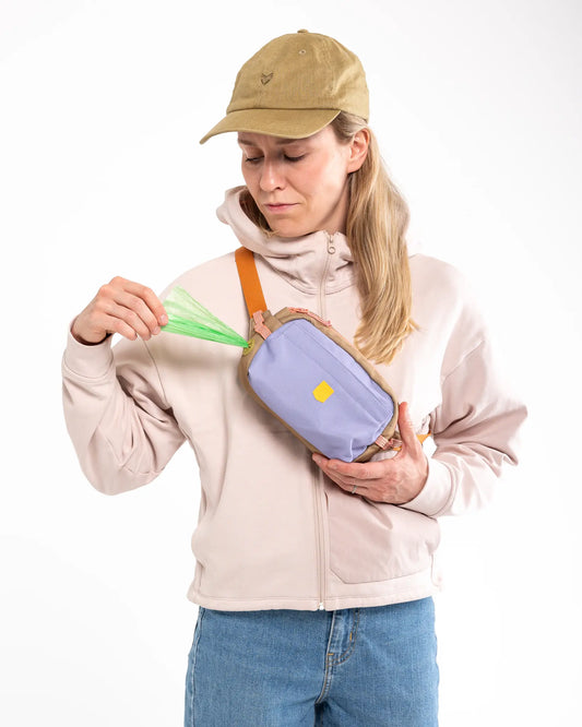 Kvindelig hundeejer trækker hundeposer ud fra Alpha 360 godbidstaske i Lavender Mix.